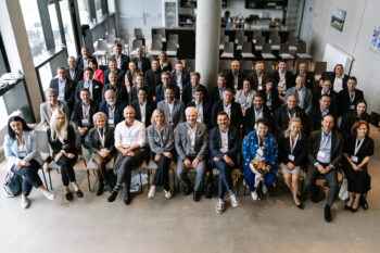 Gesamtes Gruppenfoto, alle tragen Businesskleidung und sitzen